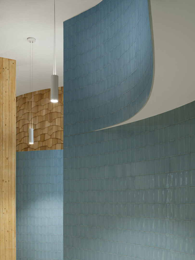 Curved blue tiled wall and hanging pendant lights with wooden paneled surfaces in a modern interior space.