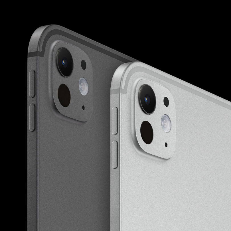 Close-up of two tablet devices, one resembling the iPad Pro in dark gray and one in silver, highlighting rear cameras and side buttons against a black background.