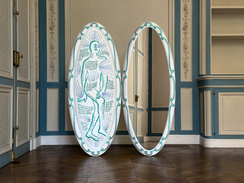 Two large, oval mirrors with decorative green borders stand side by side; one mirror features a line drawing of a human figure with text and arrows on its surface, reminiscent of sketches made on an iPad Pro.