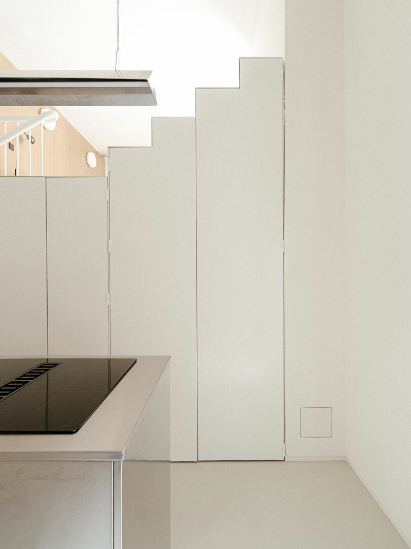 Minimalist kitchen with white stepped cabinetry, an induction cooktop on a stainless steel island, and neutral-toned walls.