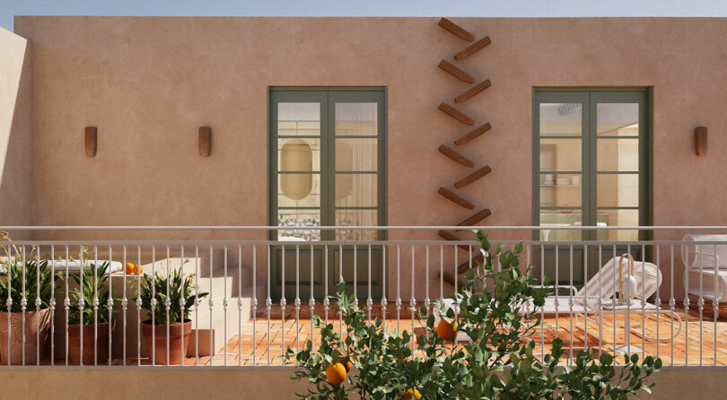 A beige building with two glass doors, potted plants, outdoor chairs, and a white railing on a sunlit terrace. Wooden beams form a zigzag pattern on the wall.
