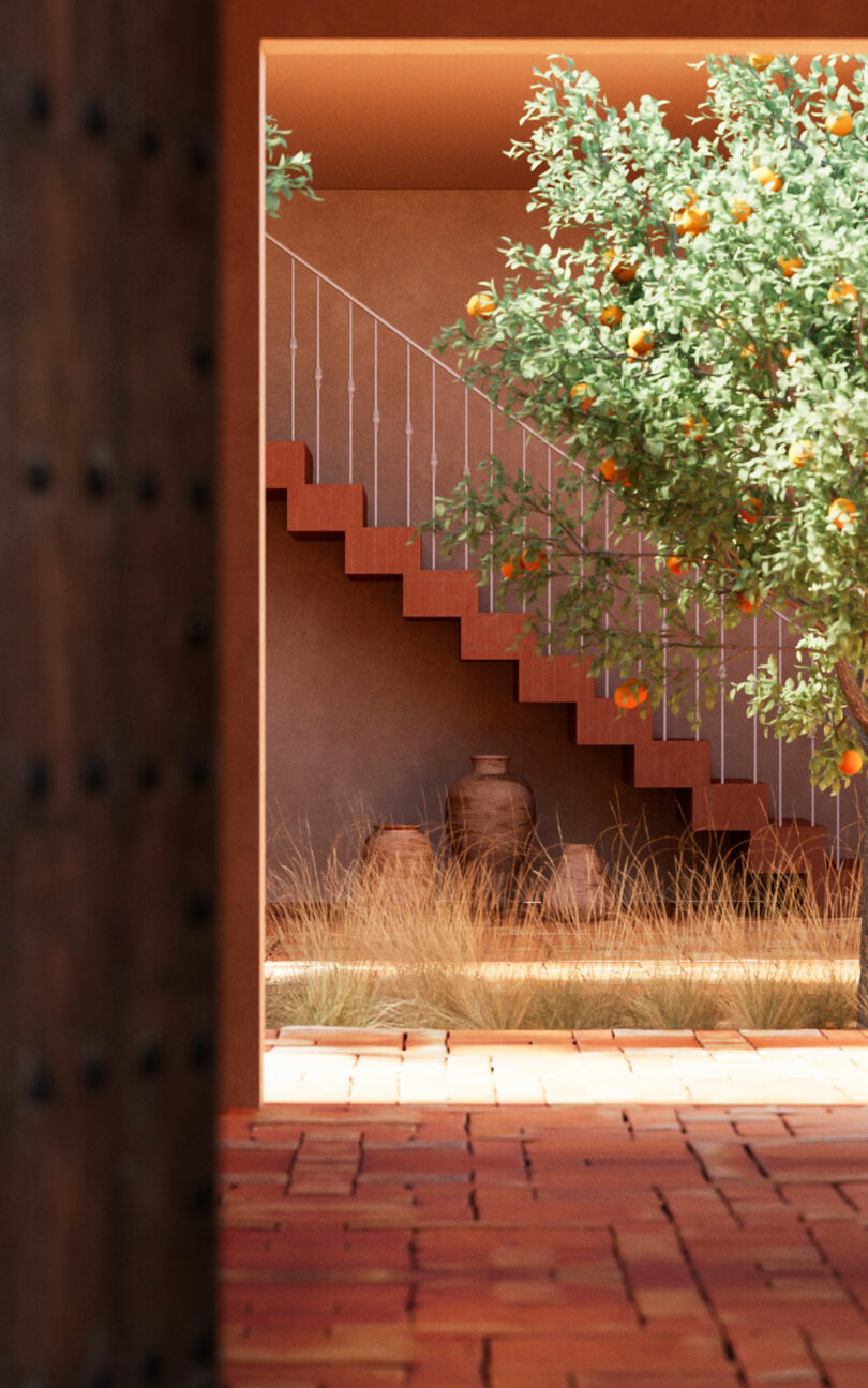 A courtyard with a terracotta tile floor, an orange tree, tall dry grass, clay pots, and an outdoor staircase with a white railing against a stucco wall.