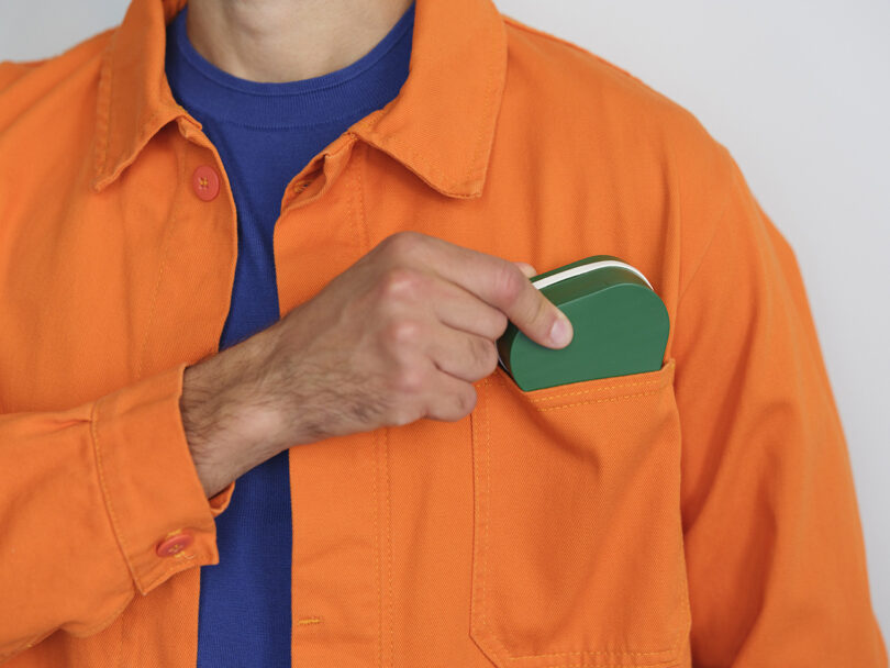 A person in an orange jacket places a green and white object into their chest pocket.