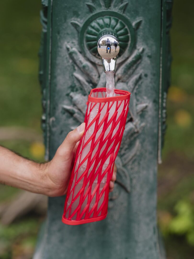 A person holds a red water bottle under a fountain spout, filling it with water.