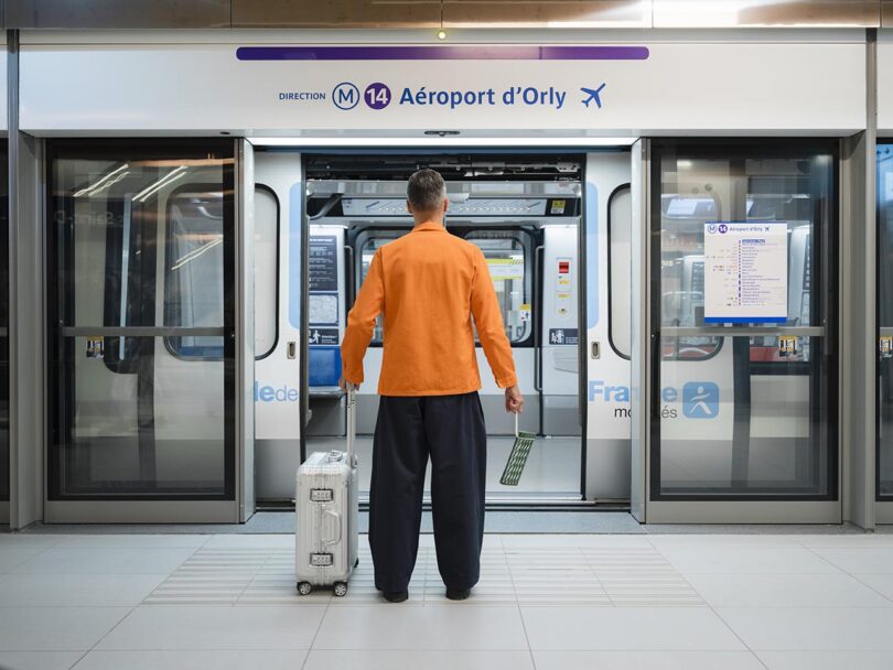 A person with a suitcase stands facing an open door of the Paris Metro Line 14 train to Orly Airport, ready to board.