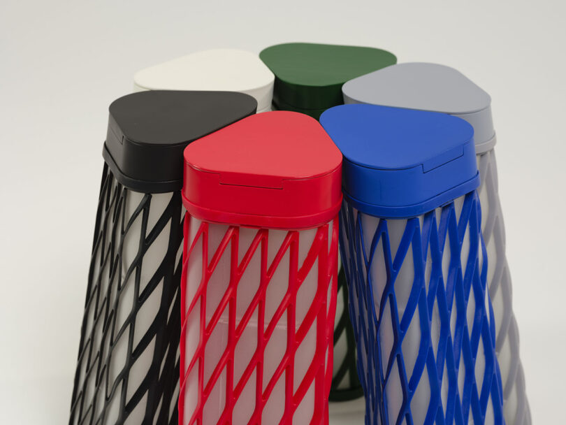 Six tall, triangular water bottles in different colors arranged in a circle, featuring a diamond-patterned mesh design on their sides.