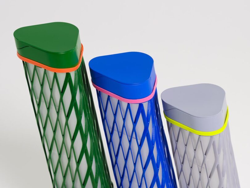 Three tall, cylindrical containers with diamond-patterned sides and triangular lids in green, blue, and gray, each with a colored band, are grouped together on a plain white background.