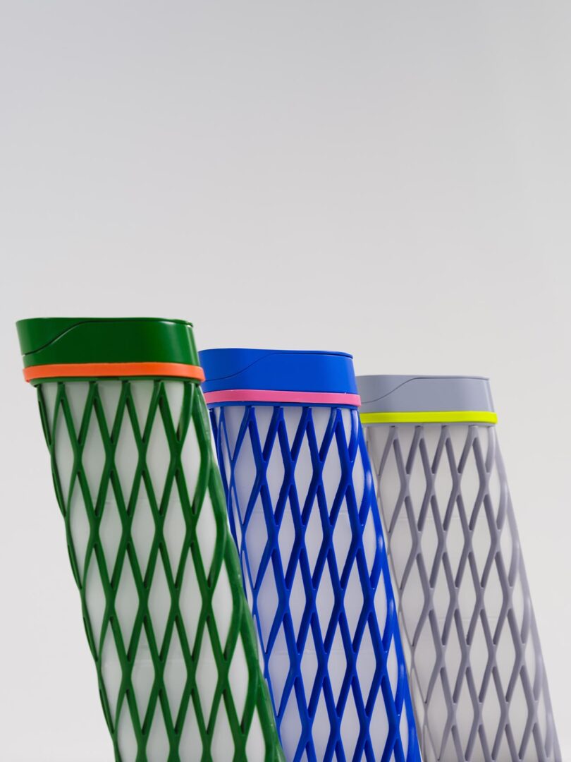 Three water bottles in green, blue, and gray with geometric mesh patterns and colored bands at the top, standing upright against a plain white background.