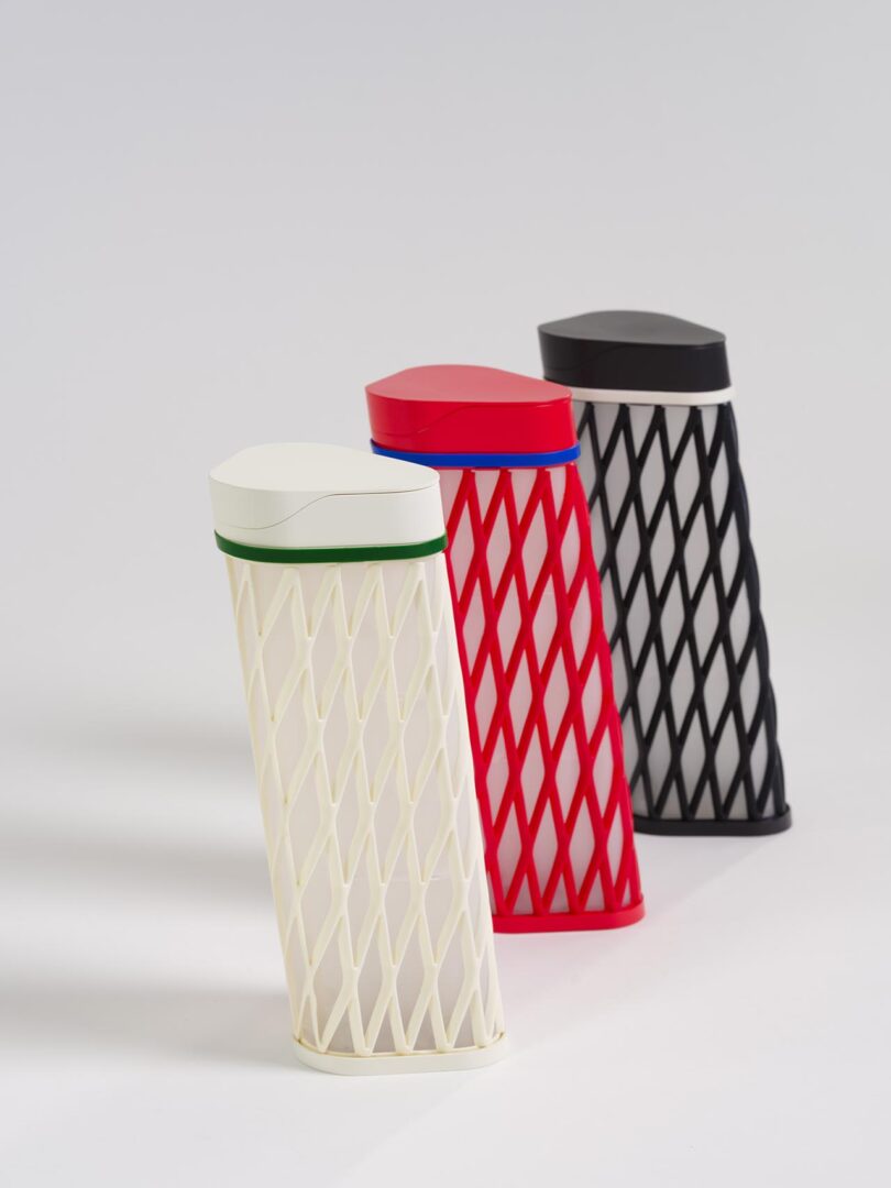 Three tall, angular containers with diamond-patterned exteriors stand upright; one is white with green, one red with blue, and one black with white.
