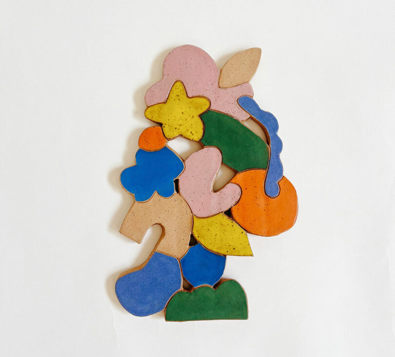 Abstract arrangement of colorful, irregularly shaped ceramic pieces, including pink, yellow, blue, green, orange, and beige, placed on a plain white background.