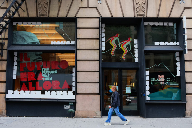 A person walks past the exterior of Poster House museum, with large modern lettering and graphics displayed on its street-facing windows.