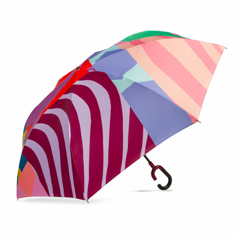 A multicolored umbrella featuring bold, abstract stripes and shapes in red, pink, purple, blue, and green tones with a black curved handle.