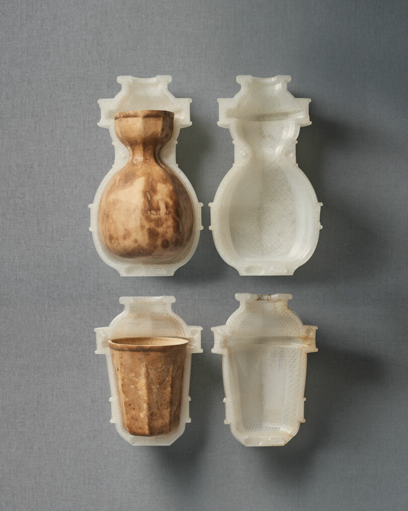 Two brown ceramic vessels displayed inside open white 3D-printed molds, arranged in two rows on a neutral gray background.