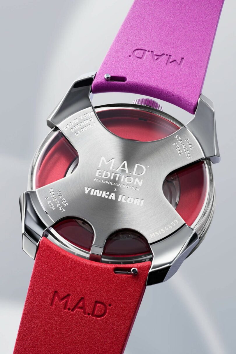 A wristwatch with a metallic backplate engraved "M.A.D. EDITION YINKA ILORI" and purple and red watch straps labeled "M.A.D