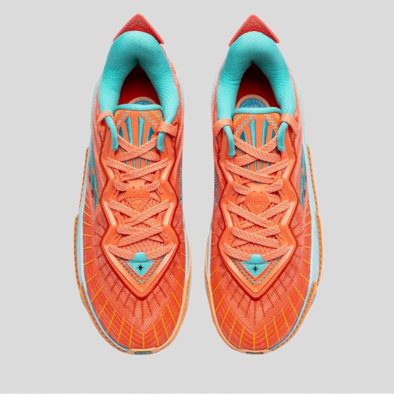 Close-up of an orange athletic shoe with blue and yellow accents, showing detailed stitching and textured sole against a plain gray background