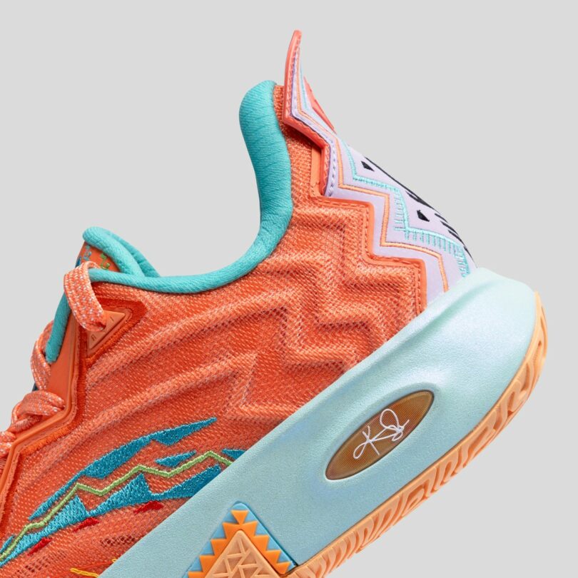 Close-up of an orange athletic shoe with blue and yellow accents, showing detailed stitching and textured sole against a plain gray background