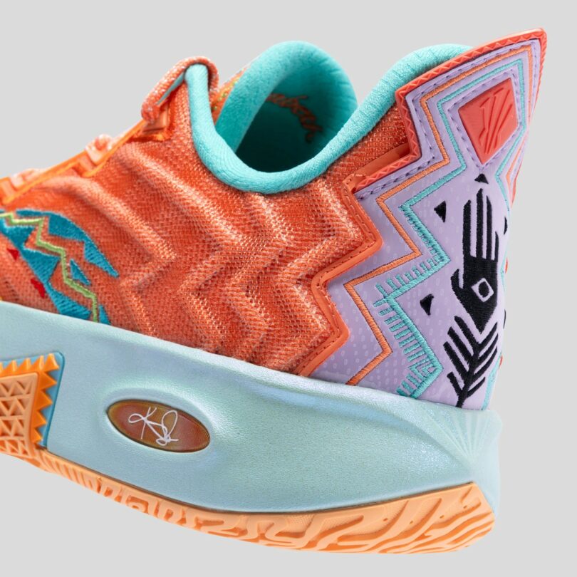 Close-up of a colorful sneaker with orange, turquoise, and purple zigzag and geometric patterns, featuring a signature on the light blue sole