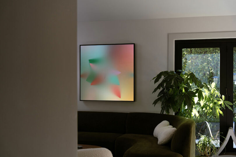 A modern living room with a curved dark sofa, green plant, and an abstract colorful painting on the wall near large black-framed windows.