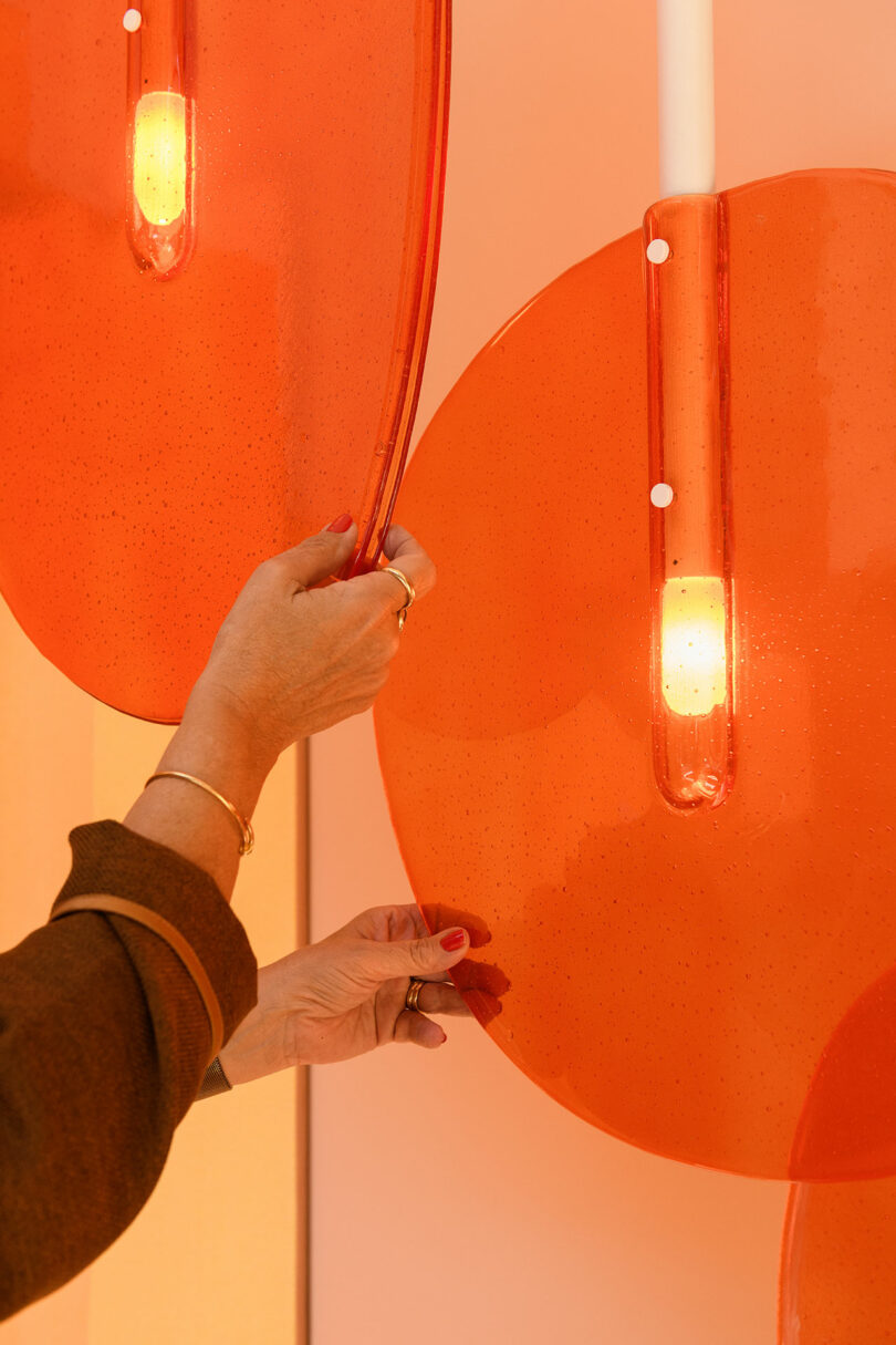 A person adjusts large, translucent orange panels surrounding vertical light fixtures mounted on a wall.
