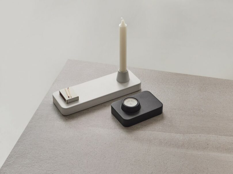 Minimalist desk accessories on a grey surface, including a white tray with a candle and sharpener, and a black tray with a tealight candle