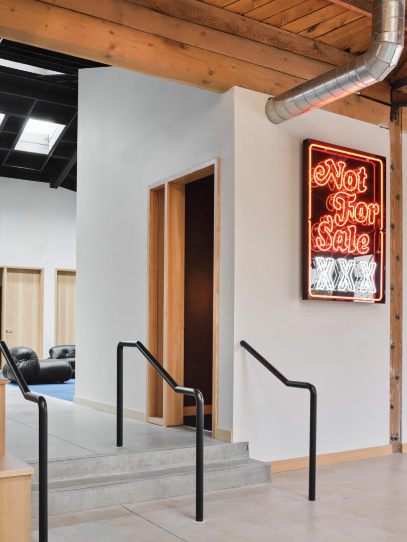 Modern interior with a small ramp and steps leading to a doorway; a neon sign on the wall reads "Not For Sale XXX." Exposed ductwork and wood beams are visible.
