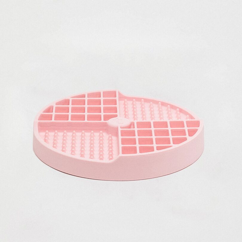 A round, pink silicone snacking tray for dogs with raised grids and textured sections placed on a plain white background
