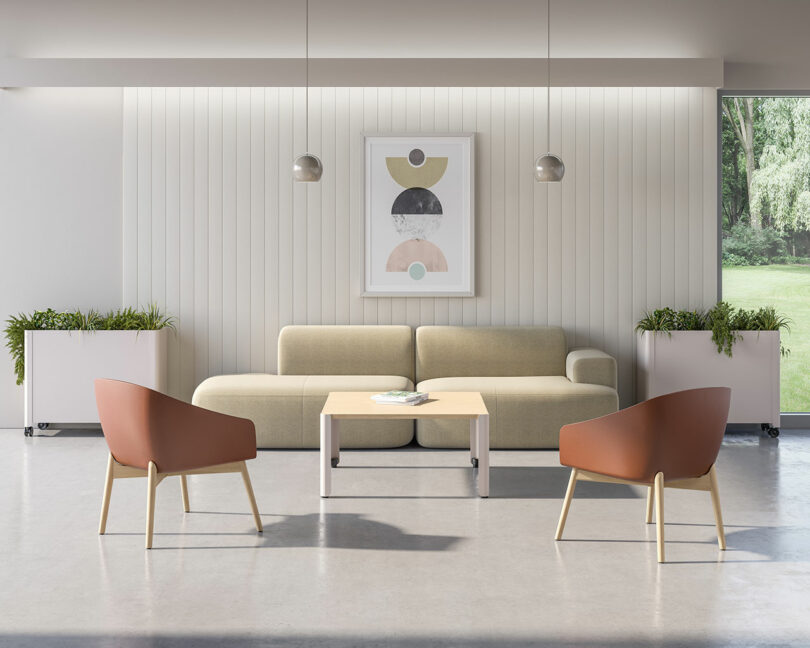 Modern living room with a beige sofa, two brown armchairs, a light wood coffee table, potted plants, pendant lights, and abstract art on a white paneled wall. Large windows show greenery outside.