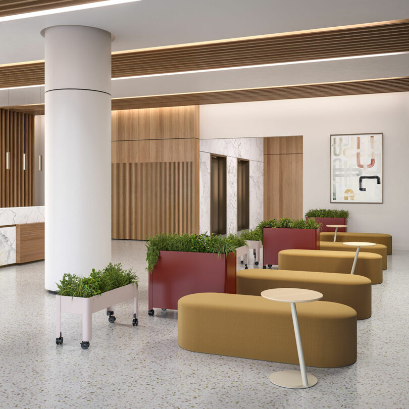 Modern lobby with mustard-colored seating, round side tables, red and white planters, large white column, wood paneling, marble accents, elevators, and abstract wall art.