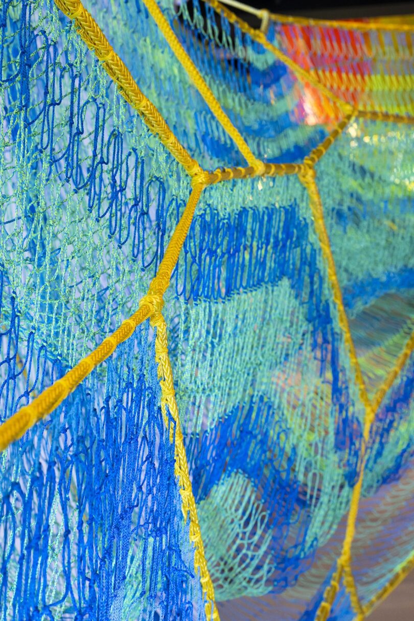Close-up of colorful netting with blue and green mesh sections bordered by yellow ropes, viewed at an angle.