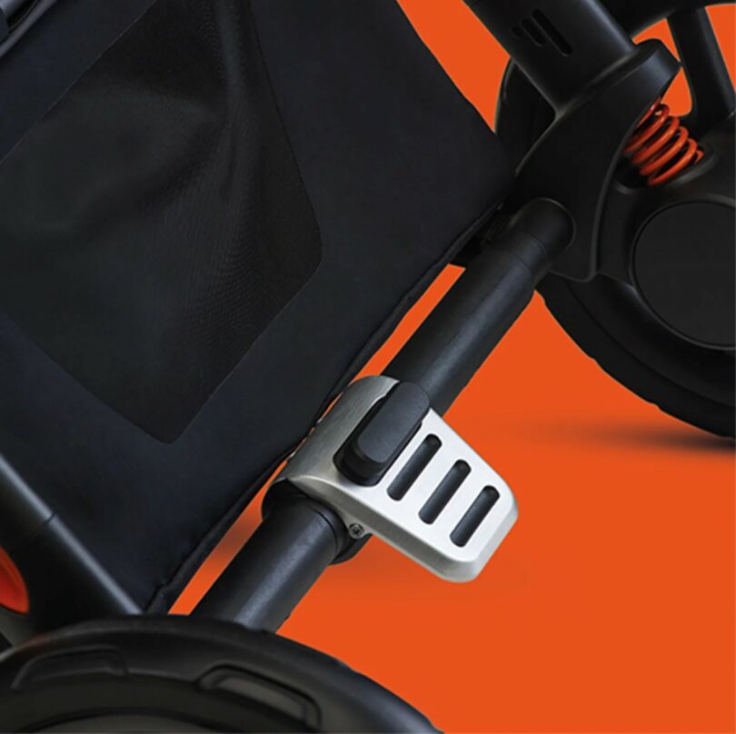 Close-up view of a Silver Cross Lamborghini stroller wheel and brake mechanism against an orange background