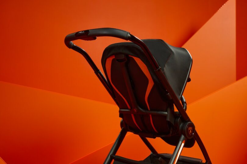 Close-up of a Silver Cross Lamborghini black stroller handle with stitching detail against an orange background.