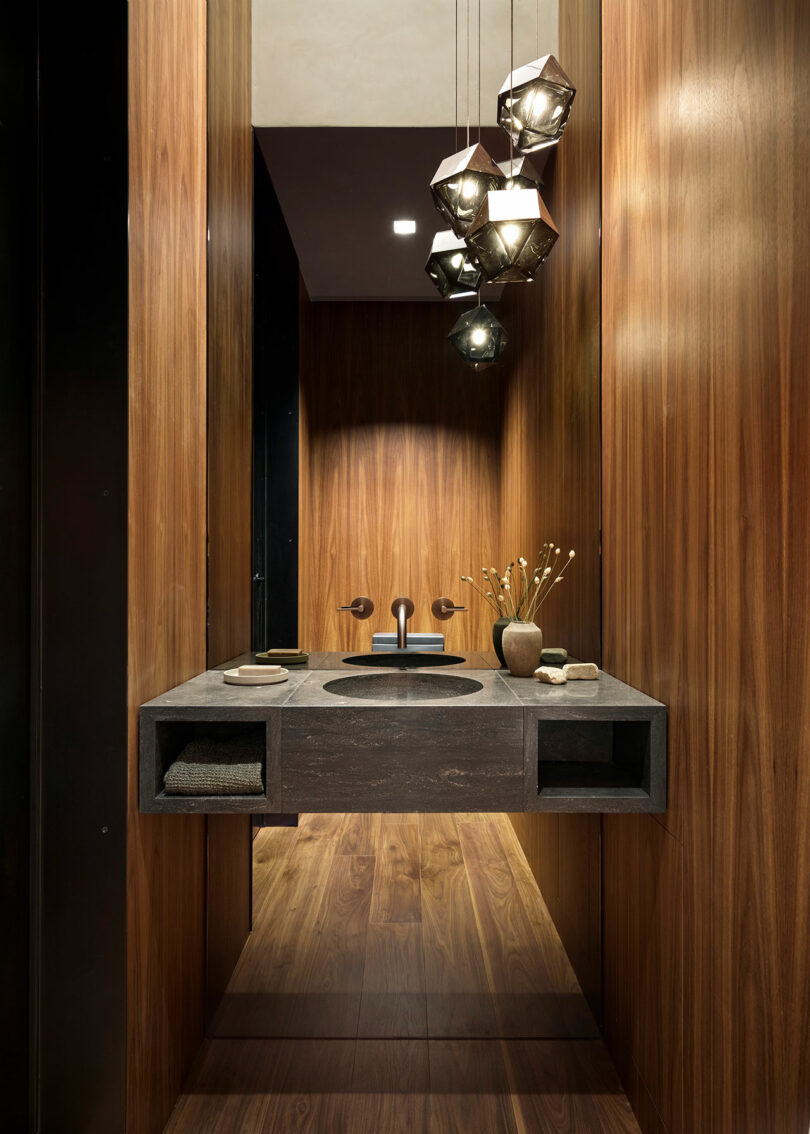 Modern bathroom with wood-paneled walls, floating black sink vanity, geometric pendant lights, and minimalist decor.