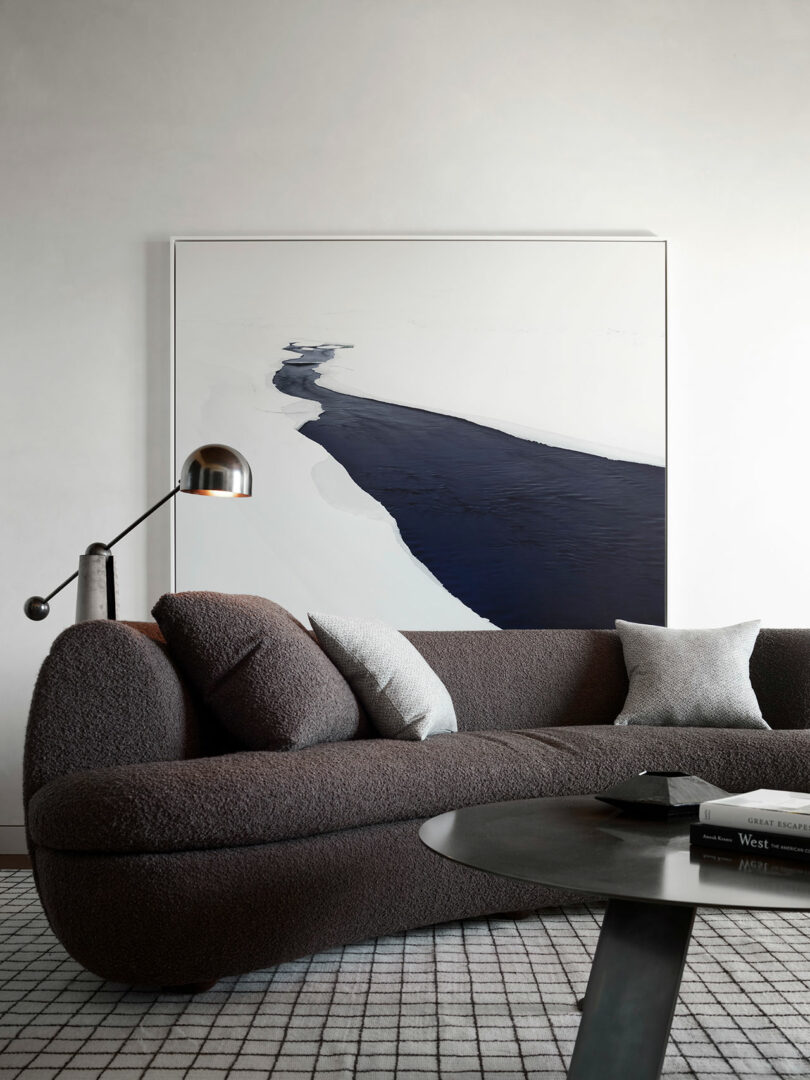 A modern living room with a dark textured sofa, monochrome cushions, round black coffee table, and a large abstract painting with navy and white tones on the wall.