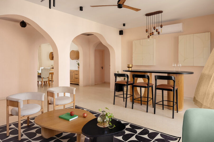 Modern open-plan living and dining area with neutral tones, arched doorways, a black kitchen island with bar stools, and contemporary decor.