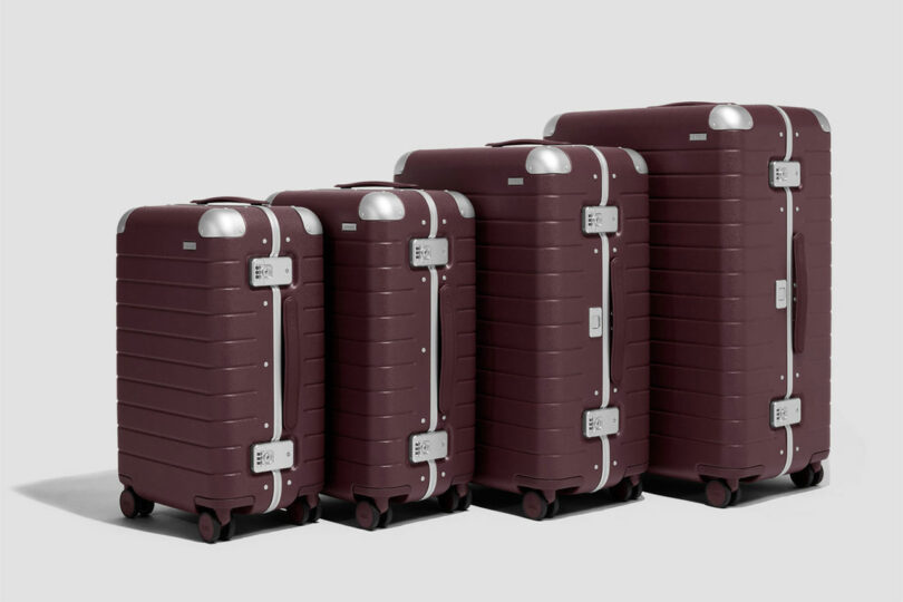 Four maroon hard-shell suitcases of varying sizes are lined up in a row against a plain background.