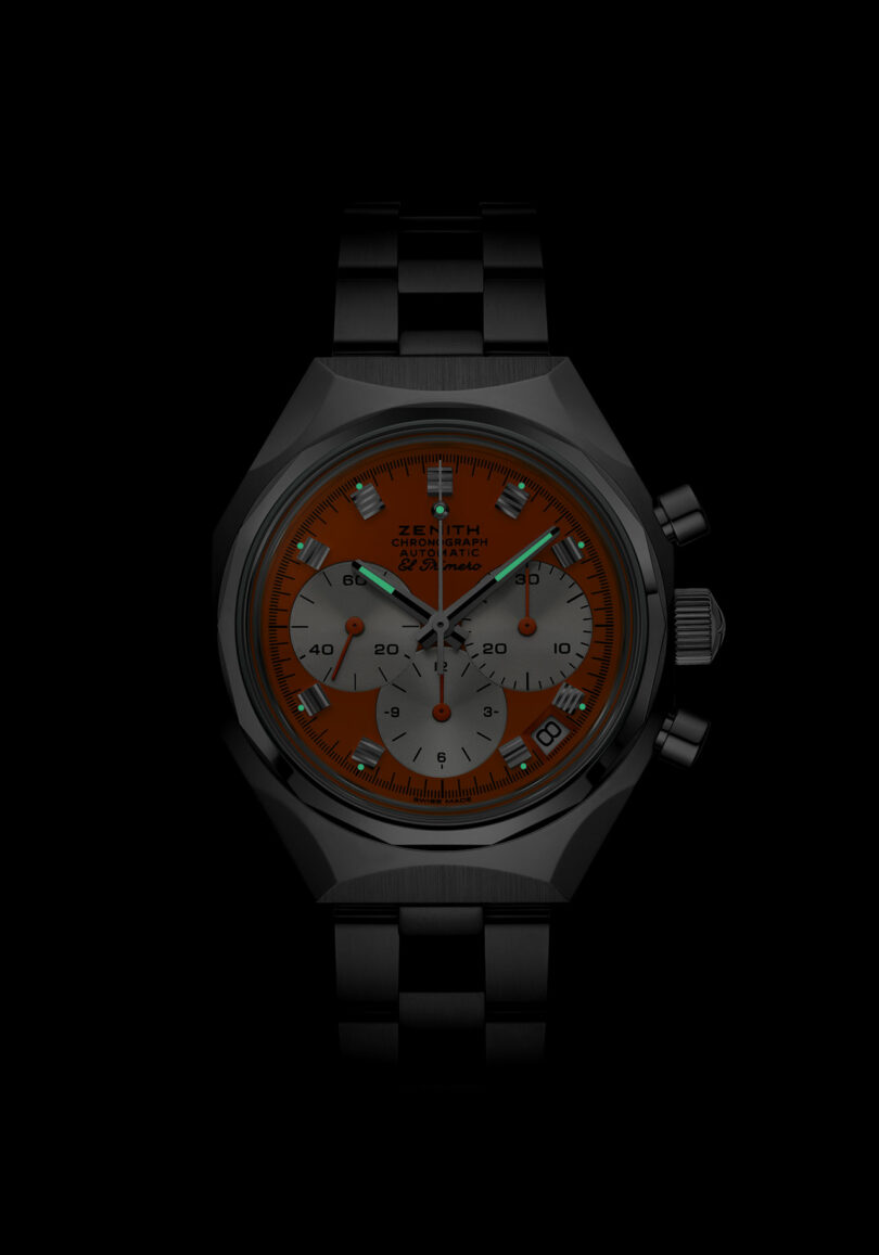 A wristwatch with a black metal band, orange dial, three silver subdials, and white hour markers, shown against a black background.