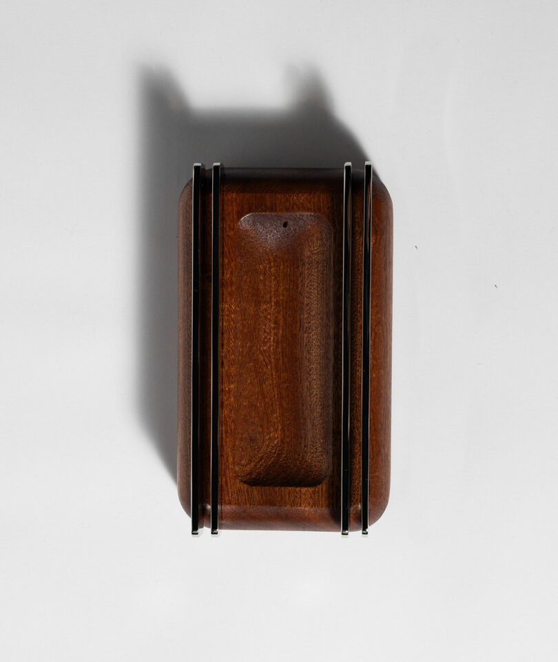 A rectangular wooden object with two parallel metal rods on each side, placed on a white surface casting shadows.